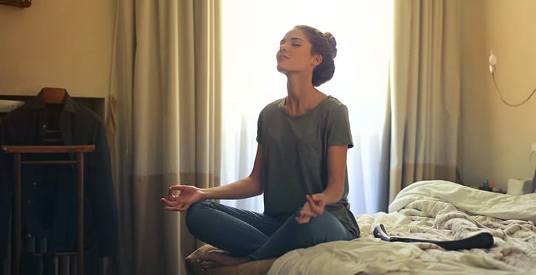 woman sitting on bed doing meditation